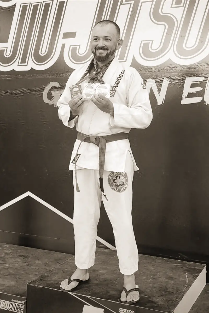 Pécora de kimono branco na premiação da Copa Jiu-Jitsu Clube, sorrindo e com medalhas na mão