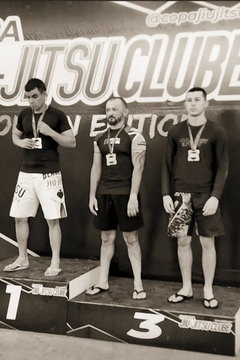 Pécora de rash guard com medalha no peito, entre outros atletas na premiação da Copa Jiu-Jitsu Clube